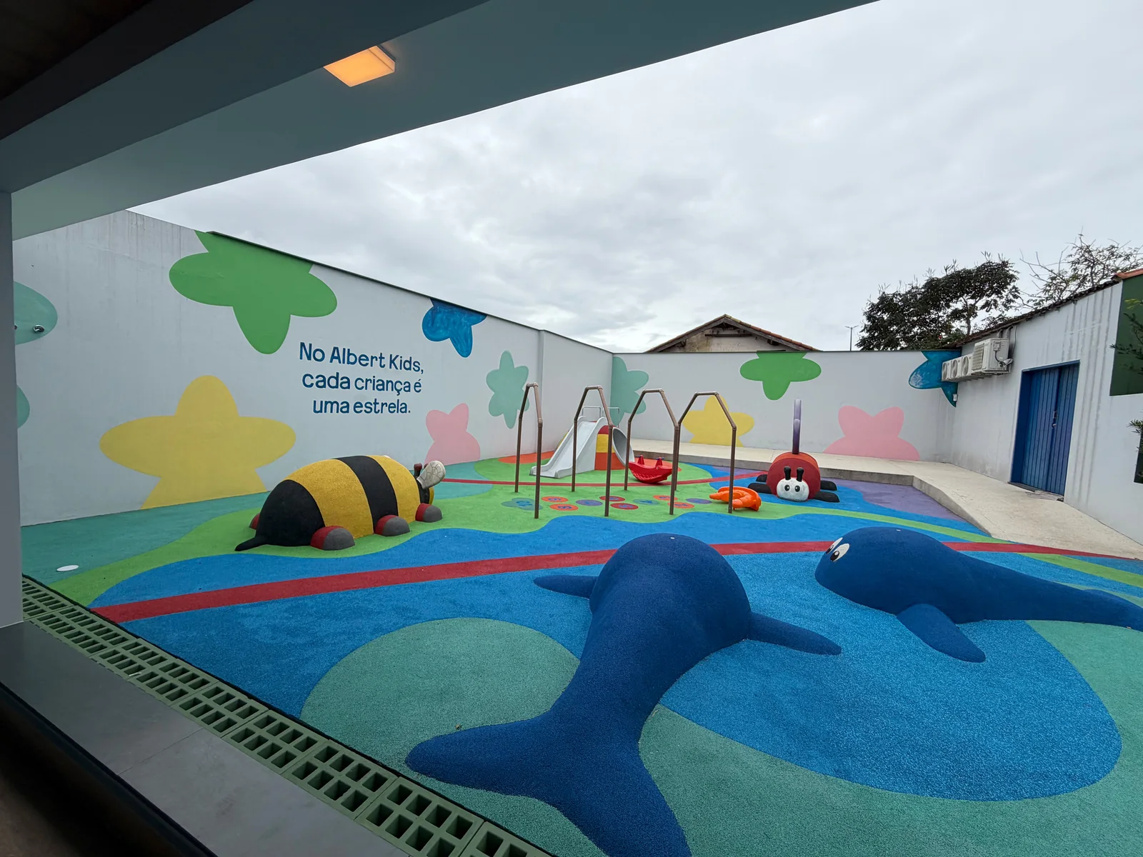 Vista do playground com brinquedos e piso colorido
